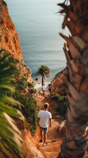 man in a white blank T-shirt walking backwards down a cliff on a beach in Portugal, around a palm tree --ar 9:16