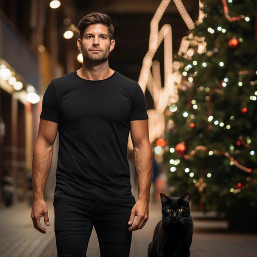 man wearing a plain black tshirt, with a brown tabby cat walking in the background, christmas background
