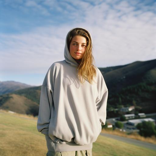 A woman in an oversized blank gray hoodie sweatshirt standing by a ski slope, shot on a 35mm film camera --s 50 --style raw