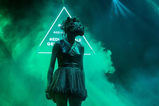 A woman with a hippo head wearing a leather dress stands on a stage, with a triangular light coming from behind. Green smoke wafts through the air. A wirefram hologram forms the words 