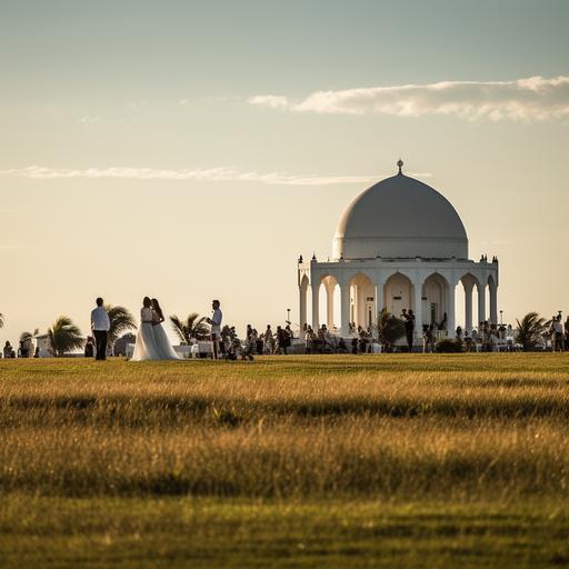 an epic 300mm shot of a white dome on columns in the grass in front of the beach. There a couple that are getting married. The couple is blurred. The female is 5'5