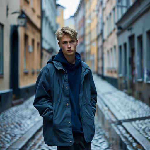 Male Model, Swedish aged 23 with blond hair. He is part of a campaign shoot for a Scandinavian brand. Model is wearing a short hooded carcoat in retro blue, fabric is a cleanmodern nylon . Very clean and minimal outfit. Underneed the jacket you can see a dark blue shirt tucked in a dark grey pleated pant. The model is standing in an street in Stockholm with minimal light grey buildings. Total picture needs to feel very natural, minimal and fresh. Shoot is in May, so lots of light and freshnes