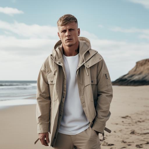 Toni Kroos on an empty Skandinavian beach. He is wearing a cargo pant with watery blue-beige camouflage print, a fresh blue shirt and on top a sand colored short nautical caban jacket. Campaign for scandinavian minimal menswear brand