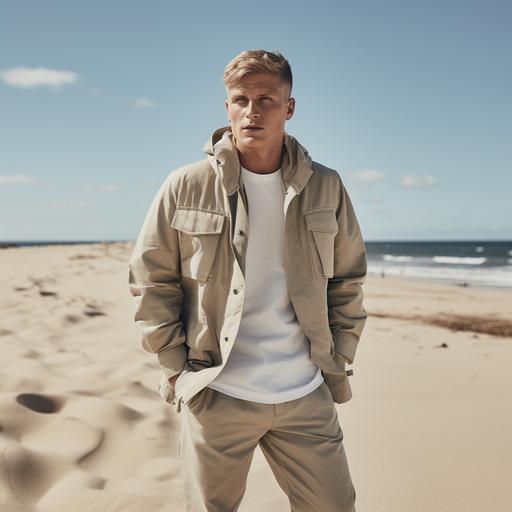 Toni Kroos on an empty Skandinavian beach. He is wearing a cargo pant with watery blue-beige camouflage print, a fresh blue shirt and on top a sand colored short nautical caban jacket. Campaign for scandinavian minimal menswear brand