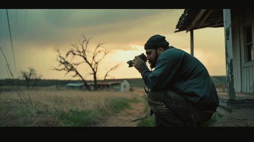 a 30 year old 210 lb hispanic male wearing a beanie is filming on his dslr camera outside in middle of the country in kansas, he has a beard and tattoos, the lighting is dramatic, the photography composition is similar to how Roger Deakins frames, --ar 16:9