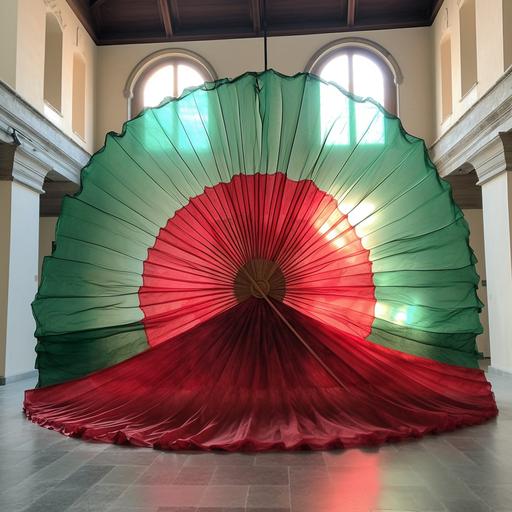 a giant spanish fan, made out of green and red layerd organza, opera set design, realistic, outdoors in a open space in saluzzo italy opera academy