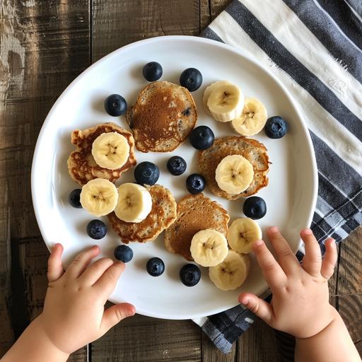 a white plate with two toddler hands holding it on the plate there's bite sized oatmeal banana blueberry pancakes