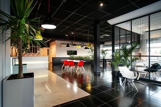 large office space, minimal modern industrial look, black flooring, black and whote tiling floor accents, piazza theme style, plants on wall, black ceiling, industrial lighting, glass office partitioning, black aluminium framed partitioning, black furniture, white contemporary office chairs, red accents, neon green accents, neon yellow accents, neon orange accents, playful but serious atmosphere, creative office environment, modern pendants lighting, lots of white space, gold accents, black and white style --v 6.0 --ar 3:2