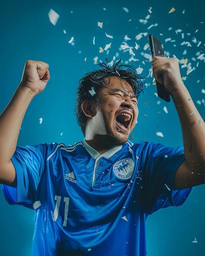 photograph of an Indonesian male in blue jersey, very happy, holding cellphone away from himself, one hand punching in the air, mobile screen spitting virtual rewards points icon, magazine cover style --ar 4:5 --v 6.0