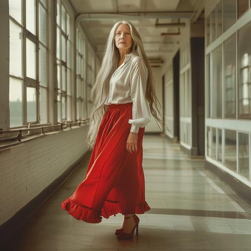 photograph,woman,Caucasian,long grey hair,red skirt,white silk blouse, heels,standing in corridor, feet apart, facing photographer, windows along one wall
