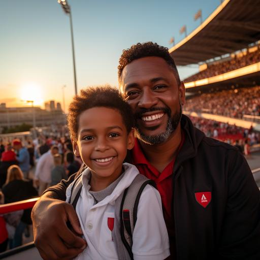 dad and his son, brown skin, both using white shirt with black collar and red logo in heart, smiling for the picture, in front a stadium entrance, in Sao Paulo Brazil, sunset light