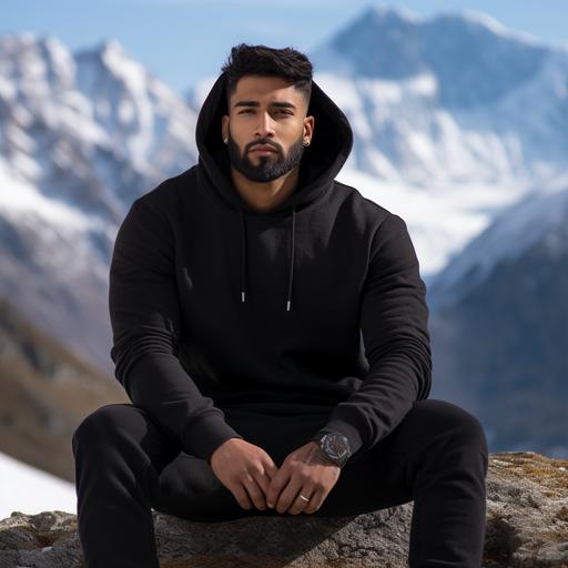 side profile photoshoot of a 6 feet tall brown Indian man wearing high quality, plain black hoodie sitting on a rock. Background is in the snow capped mountains.